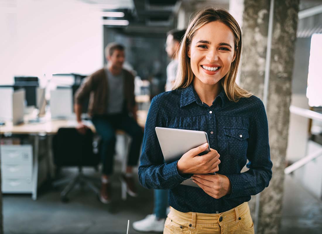 Business Owners Insurance - Portrait of a Smiling and Happy Employee in a Successful and Modern Office with Fellow Employees Blurred in the Distance