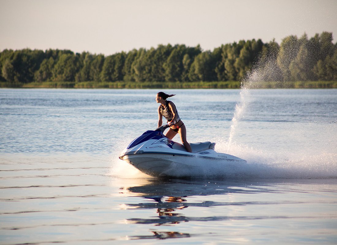 Insurance Solutions - View of a Young Woman Standing and Riding on a Jetski at Sunset on the Lake While on Vacation