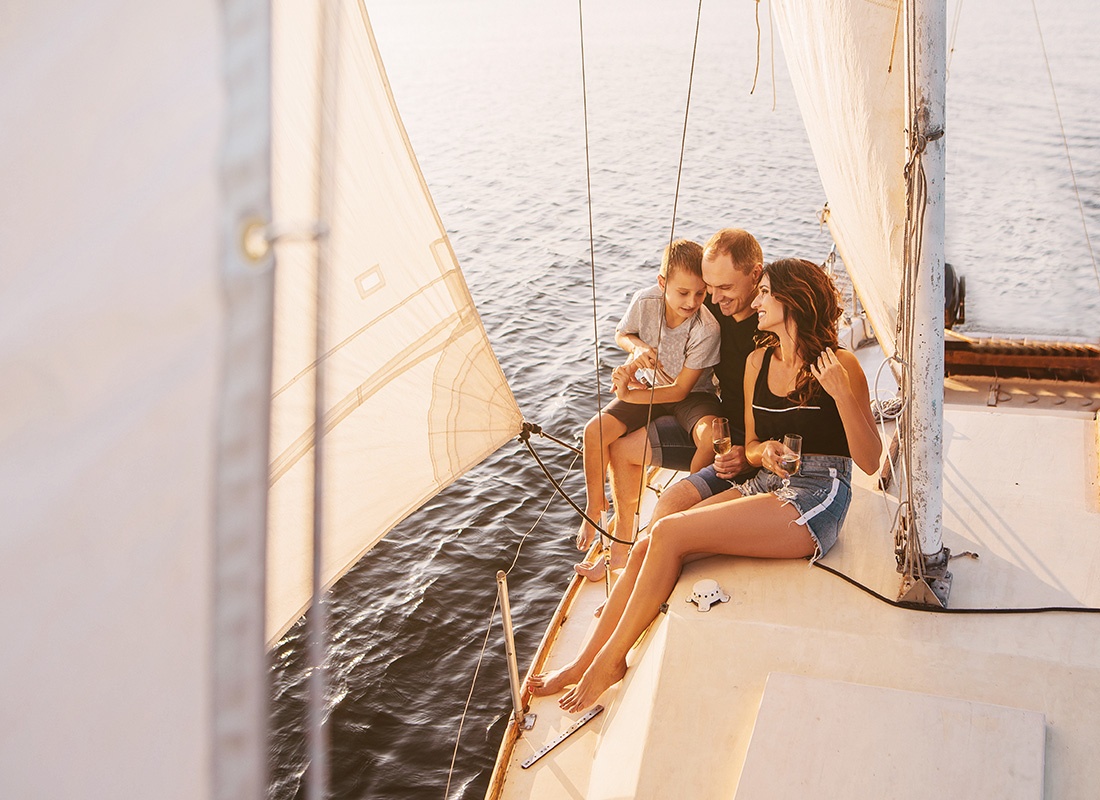Personal Insurance - Portrait of a Cheerful Family with a Son Having Fun Relaxing on a Luxury Sailboat at Sunset Out on the Lake