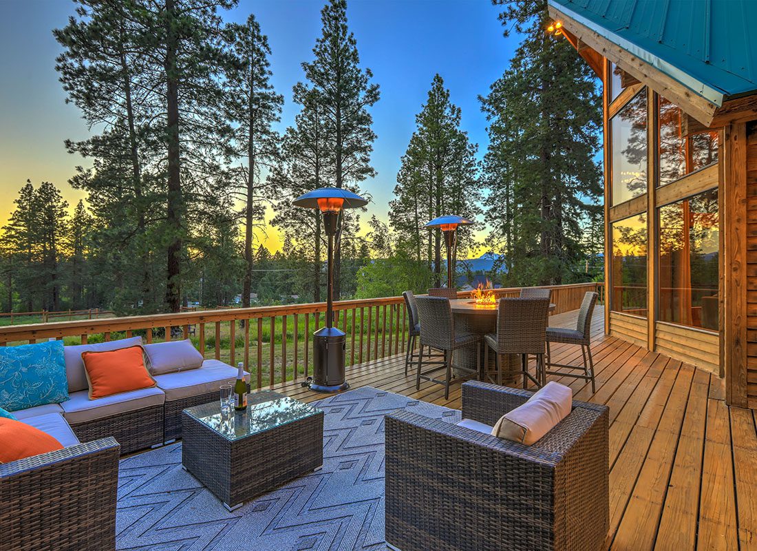 Service Center - Beautiful Sitting Area on a Wooden Deck of a Vacation Home with Patio Furniture and a Fireplace at Sunset Surrounded by Green Trees