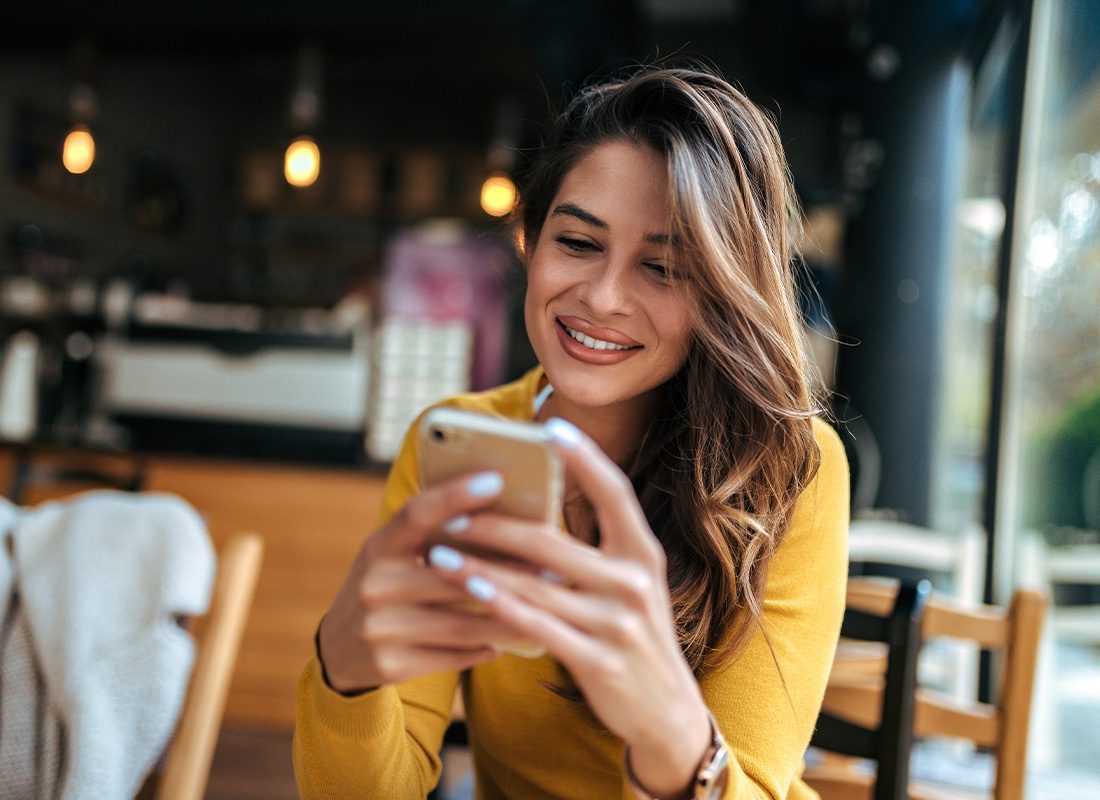 Blog - Beautiful Young Woman Reading Text Messages on Mobile Phone at the Cafe